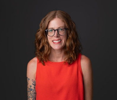 Headshot of a woman with shoulder length red hair, glasses, and a sleeveless red shirt