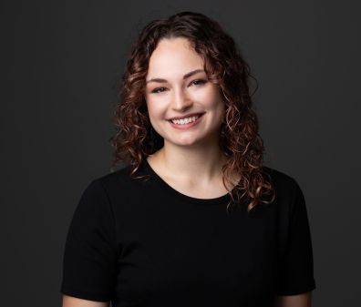 Headshot of a woman with curly brown hair in a scoop neck black shirt