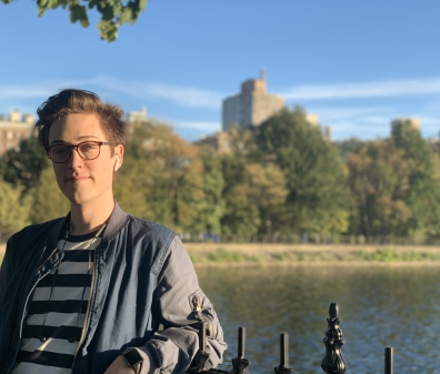 Photo of a man with glasses and short hair in a striped shirt and jacket posed in front of a lake