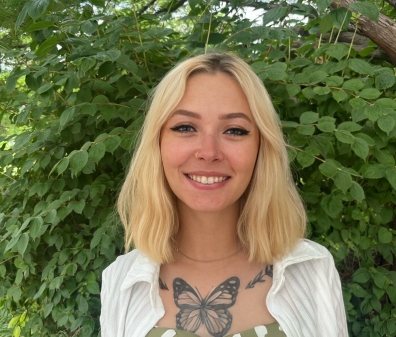 headshot of a person with shoulder-length blonde hair wearing a green and white shirt and white cardigan