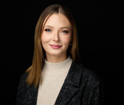 Headshot of a woman with shoulder length dark blonde hair wearing a tan sweater and a black blazer