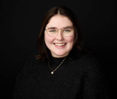 Headshot of a woman with short hair and glasses wearing a black sweater with a pearl necklace