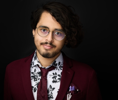 Headshot of a person in a burgundy blazer, tie, and white and black button up shirt